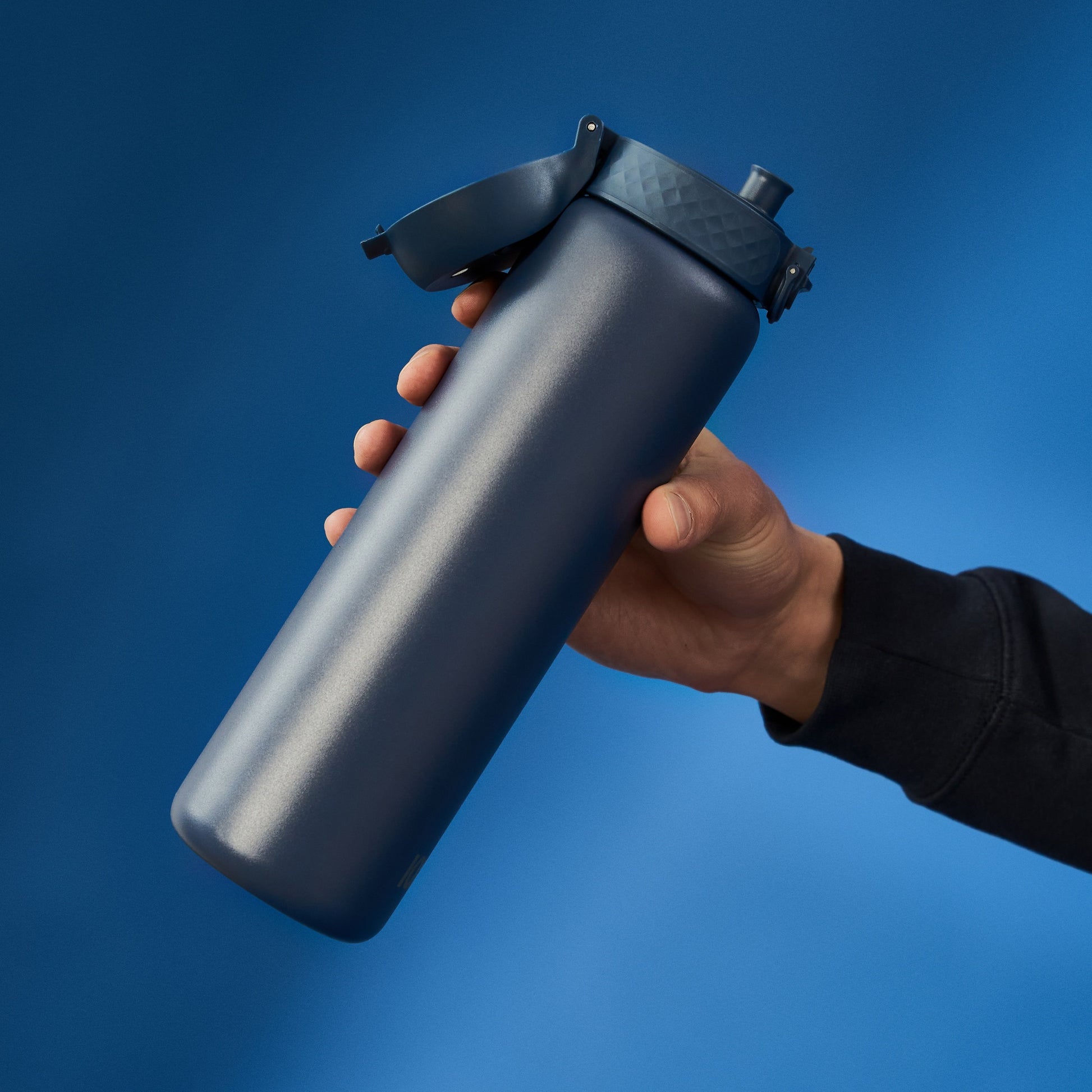 A dark-blue water bottle is held by a hand, against a blue background.