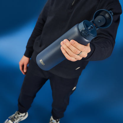 A dark-blue ION8 water bottle is held, its lid open; a person wearing dark clothing holds it against a blue background.