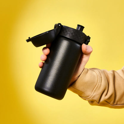 A hand holds a black insulated bottle with an open flip-top lid against a bright yellow background.