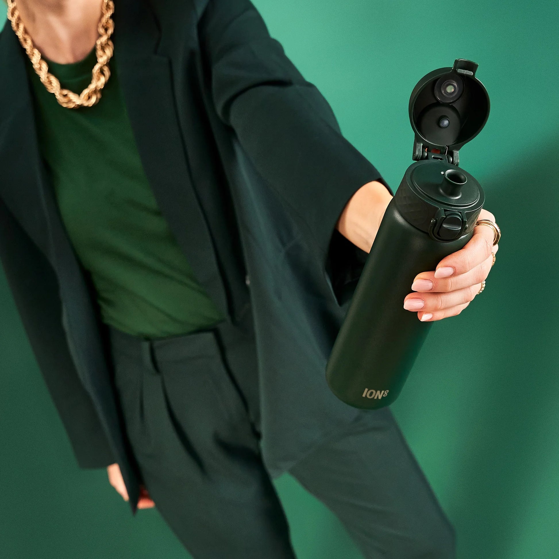 A person wearing a dark green outfit extends an open black thermos labeled "ION8" toward the camera against a matching green background.