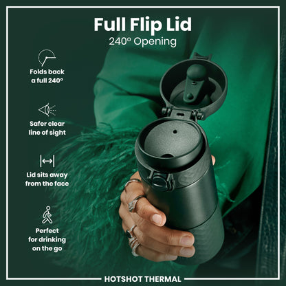 A dark-green thermal cup, with its full flip lid open 240 degrees, is held in a hand. The lid is designed for safe, on-the-go drinking. The background is a dark-green fabric. Full Flip Lid. 240° Opening. HOTSHOT THERMAL.