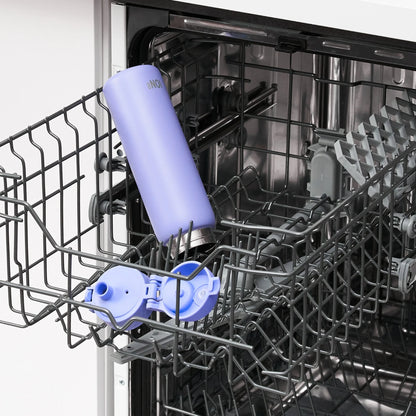 A light purple insulated bottle labeled "ONE" stands upright in a dishwasher rack next to a lid with flaps open inside a clean, empty kitchen dishwasher.