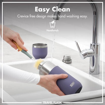 A hand scrubs a travel flask with a brush under a running kitchen faucet. Text: Easy Clean Crevice free design makes hand washing easy. Handwash. Travel Flask.